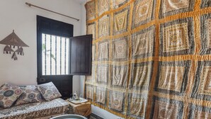 A room with a patterned sofa, a small round table, a wall-mounted TV, and a large decorative tapestry.