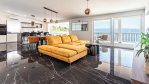 Un espace de vie moderne comprenant un canapé, une table à manger et des chaises, une cuisine avec un coin repas, et de grandes fenêtres offrant une vue dégagée.
