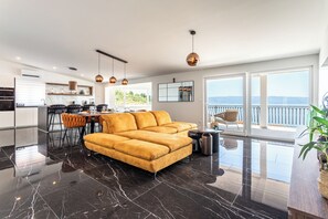 Ein modernes Wohnzimmer mit einer Couch, einem Esstisch und Stühlen, eine Küche mit Essbereich sowie große Fenster mit Blick.