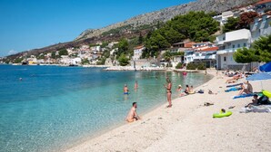 Une plage avec une eau claire, des gens qui se baignent et qui prennent des bains de soleil, et des bâtiments qui bordent la côte.
