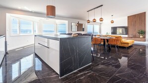 Une cuisine moderne avec un îlot en marbre, un coin repas doté d’un canapé jaune et de grandes fenêtres offrant une vue dégagée.
