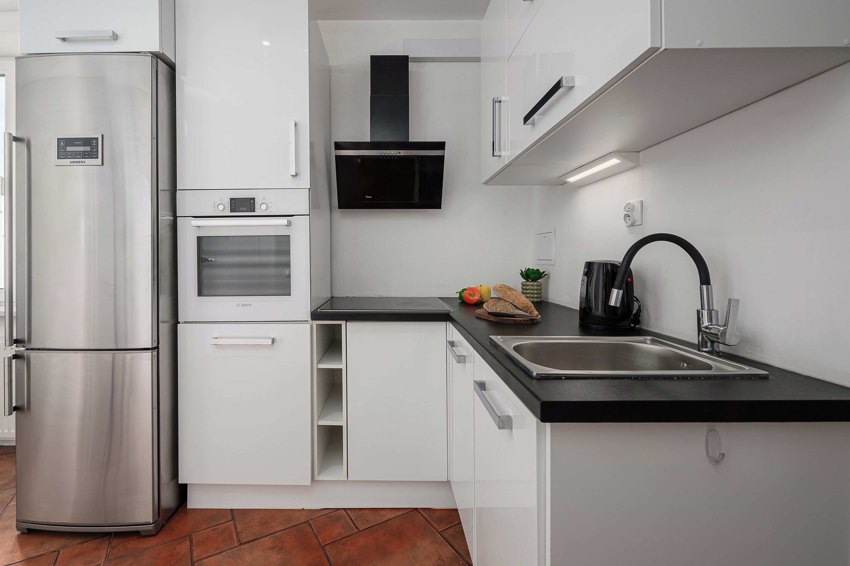 A modern kitchen with a stainless steel refrigerator, oven, and black range hood.
