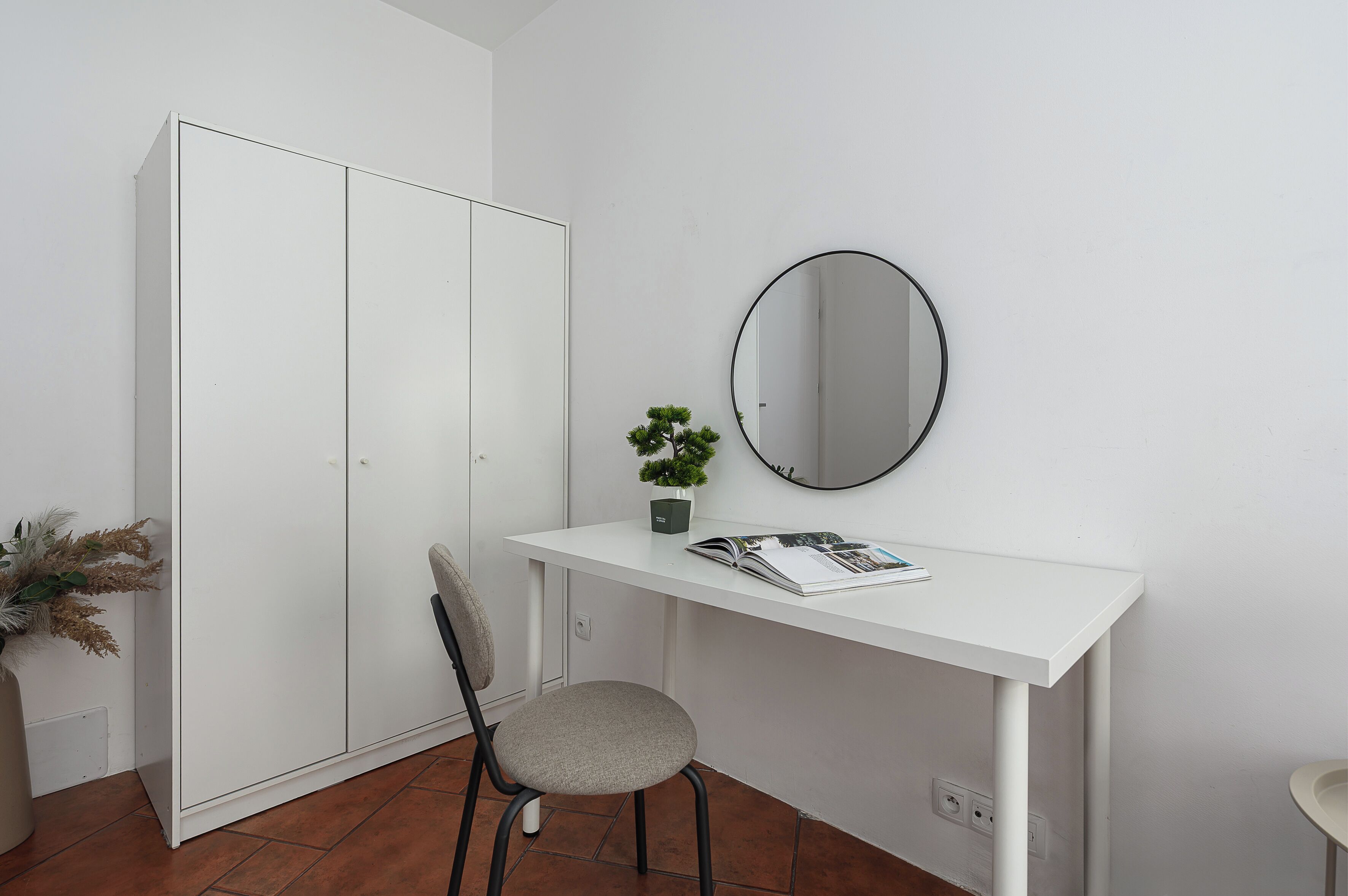 A white wardrobe, a chair, a small table with a mirror, and a potted plant.