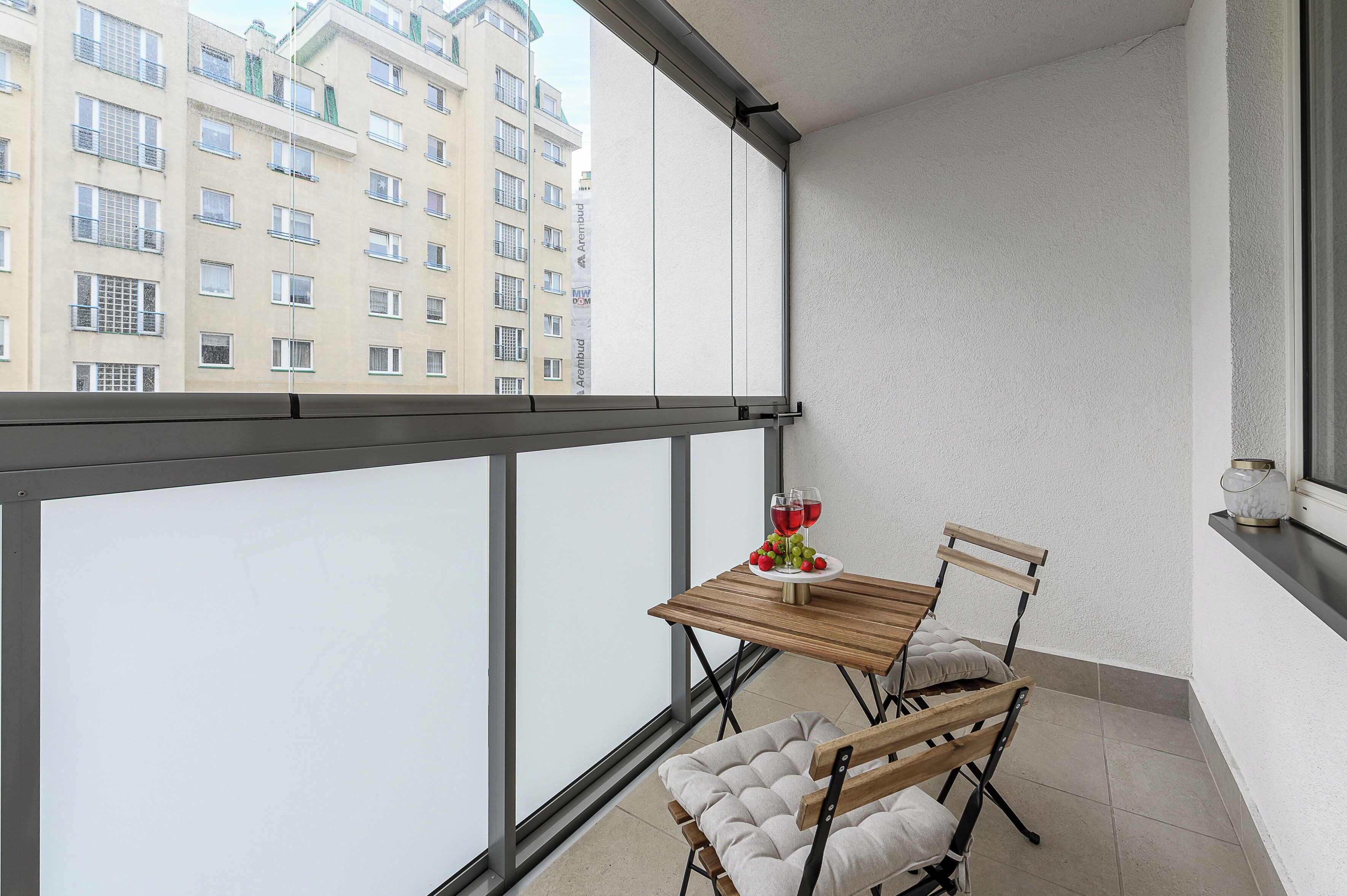 Ein Balkon mit Tisch, Stühlen und einem Fenster mit Blick auf ein Gebäude.