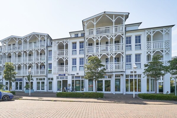 Ein mehrstöckiges Hotel mit weißer Fassade, mehreren Balkonen und einer gepflasterten Eingangsbereiches.