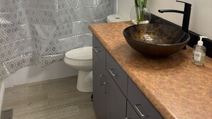 A bathroom with a patterned shower curtain, a toilet, a sink with a large bowl, a mirror, and a vase with flowers. - Cozy farmhouse retreat (Sherwood park)