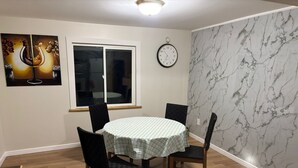 Un coin repas avec une table ronde, quatre chaises, une horloge et une fenêtre.