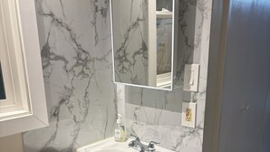 Une salle de bain avec un lavabo blanc, un miroir et des murs à motifs de marbre.