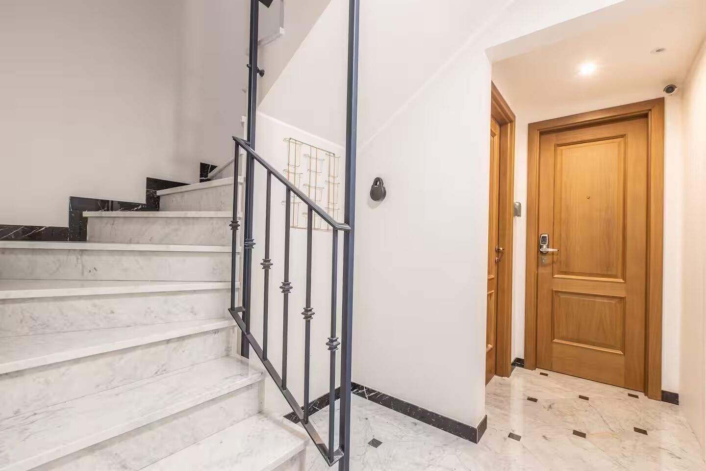 Un escalier avec une rampe en métal, une porte en bois et un mur blanc.