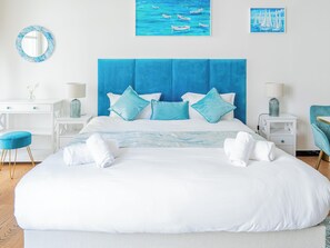 Ein Schlafzimmer mit einem großen Bett, zwei Nachttischen, einem Beistelltisch, einem Sessel und Kunstwerken an den Wänden.