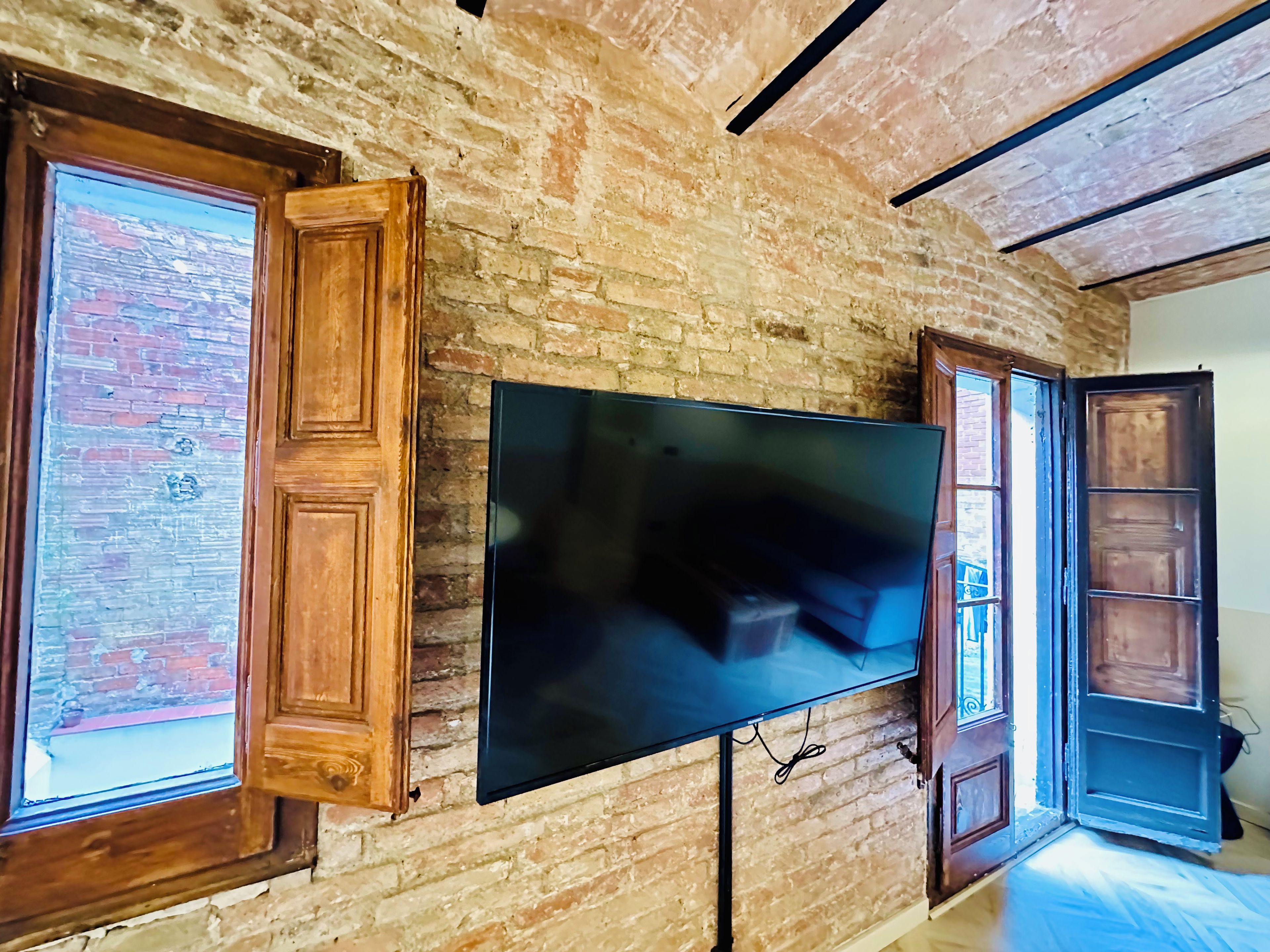 Ein Zimmer mit einer Backsteinwand, an der ein großer Flachbildfernseher angebracht ist, und Holztüren mit Glasfeldern.