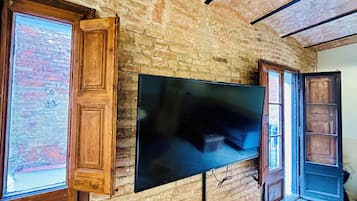 Ein Zimmer mit einer Backsteinwand, an der ein großer Flachbildfernseher angebracht ist, und Holztüren mit Glasfeldern.