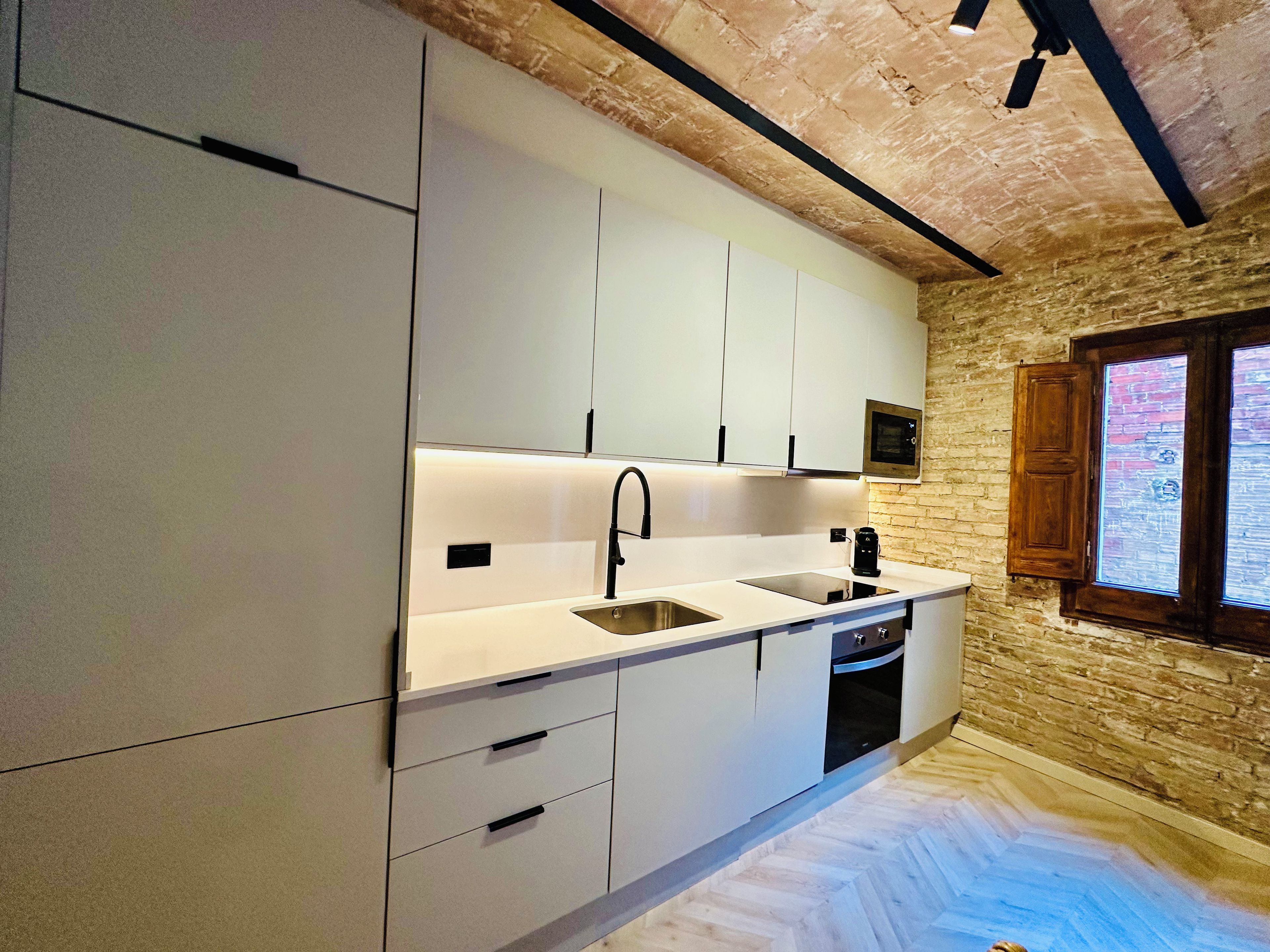 Eine moderne Küche mit weißen Schränken, einem eingebauten Backofen und einem Fenster mit Holzläden.