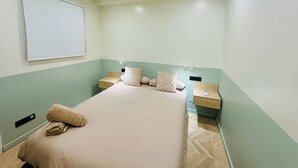 Habitació d'hotel amb un llit, dues taules de nit, un televisor penjat a la paret i un interruptor de llum.