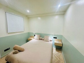 Una habitación de hotel con una cama, dos mesitas de noche, un televisor montado en la pared y un interruptor de luz.