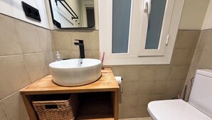 Un bany amb un rentapeus blanc, un armari de tocador de fusta, una cistella de vímet i un vàter blanc.