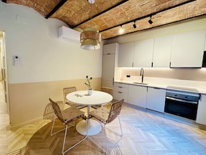 Una cocina moderna con armarios blancos, horno integrado y un comedor con mesa redonda y cuatro sillas.