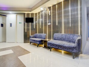 A lobby with a reception desk, two sofas, a flat-screen TV, and a patterned wall. - Saver Single Near Max Hospital (New Delhi)