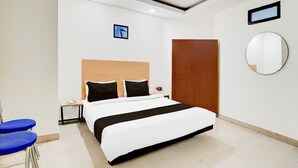 A modern hotel room with a large bed, a wooden wardrobe, a round mirror, and a small table with a chair. - Saver Single Near Max Hospital (New Delhi)