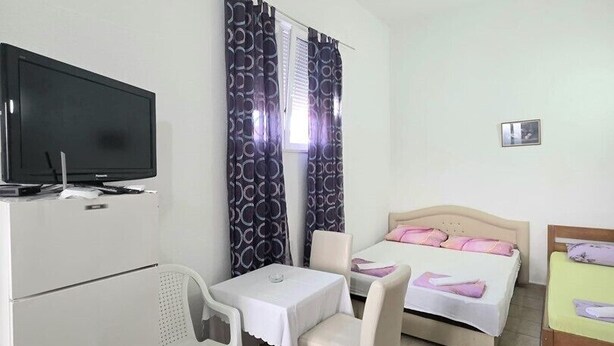 Una stanza piccola e pulita con un letto, una scrivania, una sedia, un televisore e tende.
