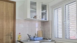 Una cucina compatta con mobili bianchi, un lavello e una finestra con persiane.