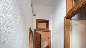 Un corridoio stretto con stipiti in legno, pavimento tappezzato e un letto visibile in lontananza.