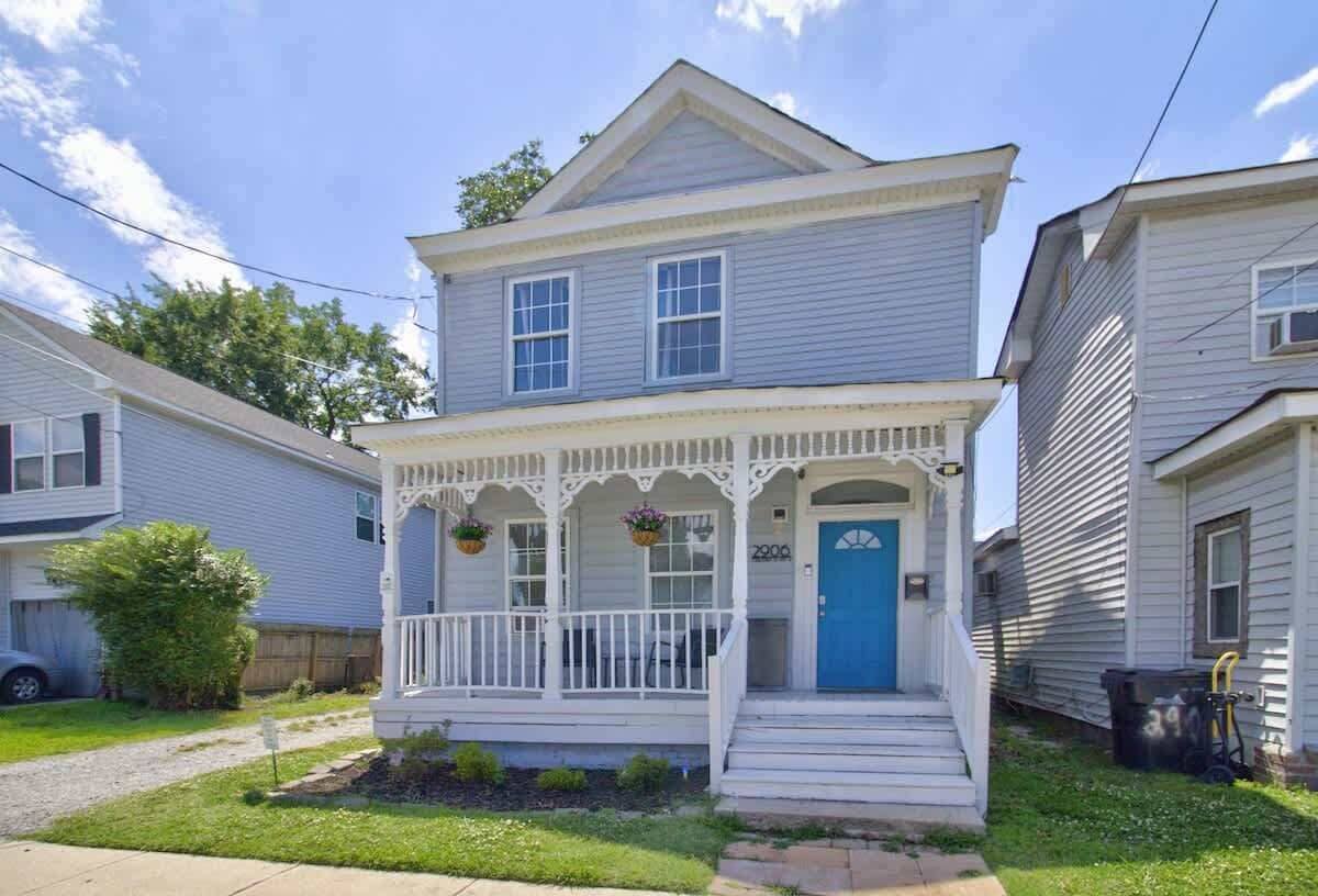 Une maison à deux étages avec un porche à l’avant, une porte bleue et un petit jardin.