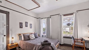 Ein Schlafzimmer mit Bett, Schreibtisch, Stuhl, einem Fenster mit Vorhängen und einer Tür.
