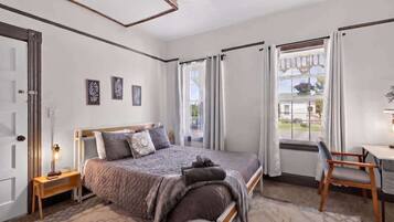 Une chambre à coucher avec un lit, un bureau, une chaise, une fenêtre avec des rideaux et une porte.