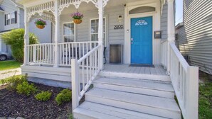 Eine weiße Veranda mit einer blauen Tür, darüber die Hausnummer '2906', und ein hängender Blumenkorb.