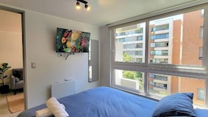 Een slaapkamer met een groot raam, een bed, een televisie en een radiator.