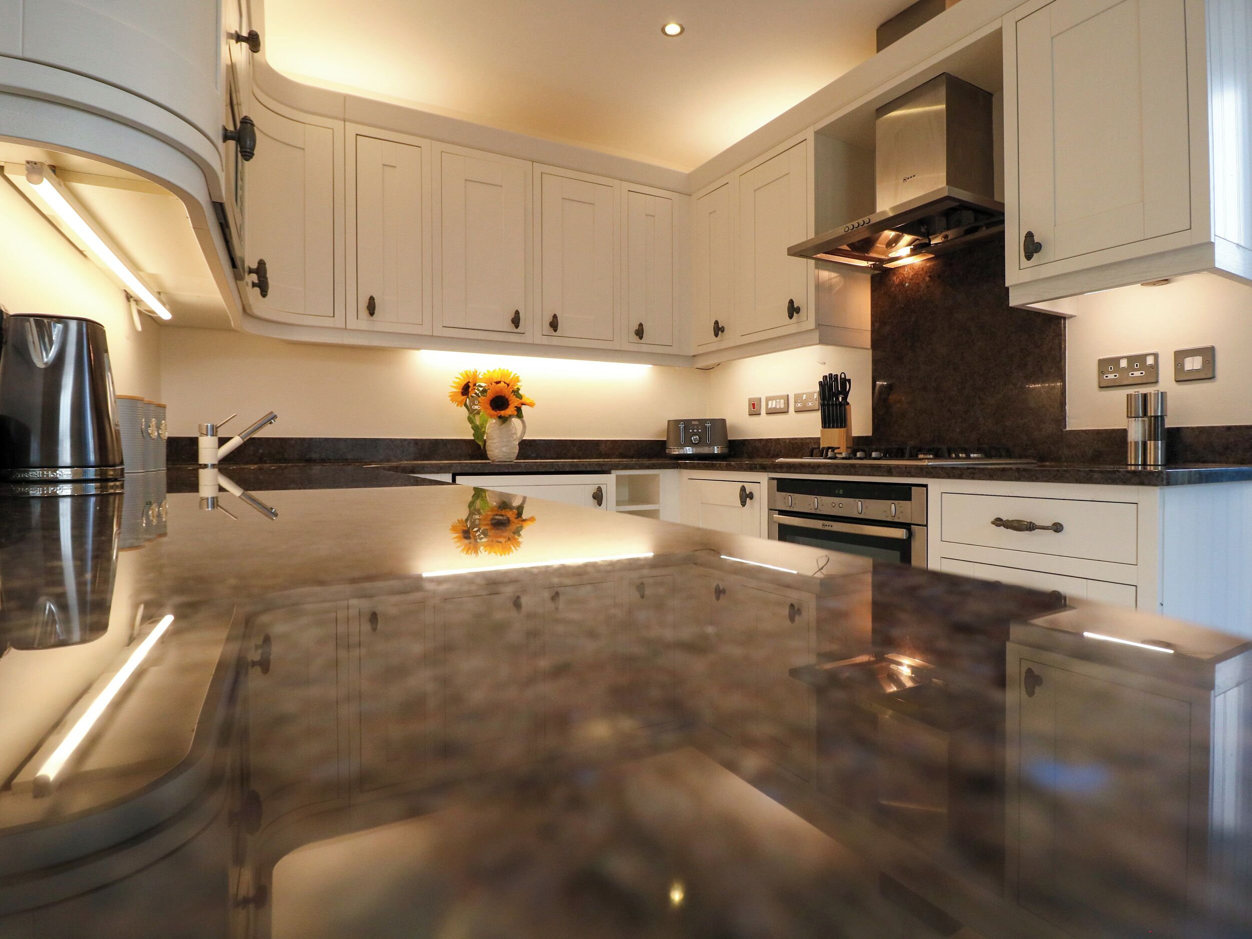 A modern kitchen with white cabinets, a central island, stainless steel appliances, and a vase with sunflowers.