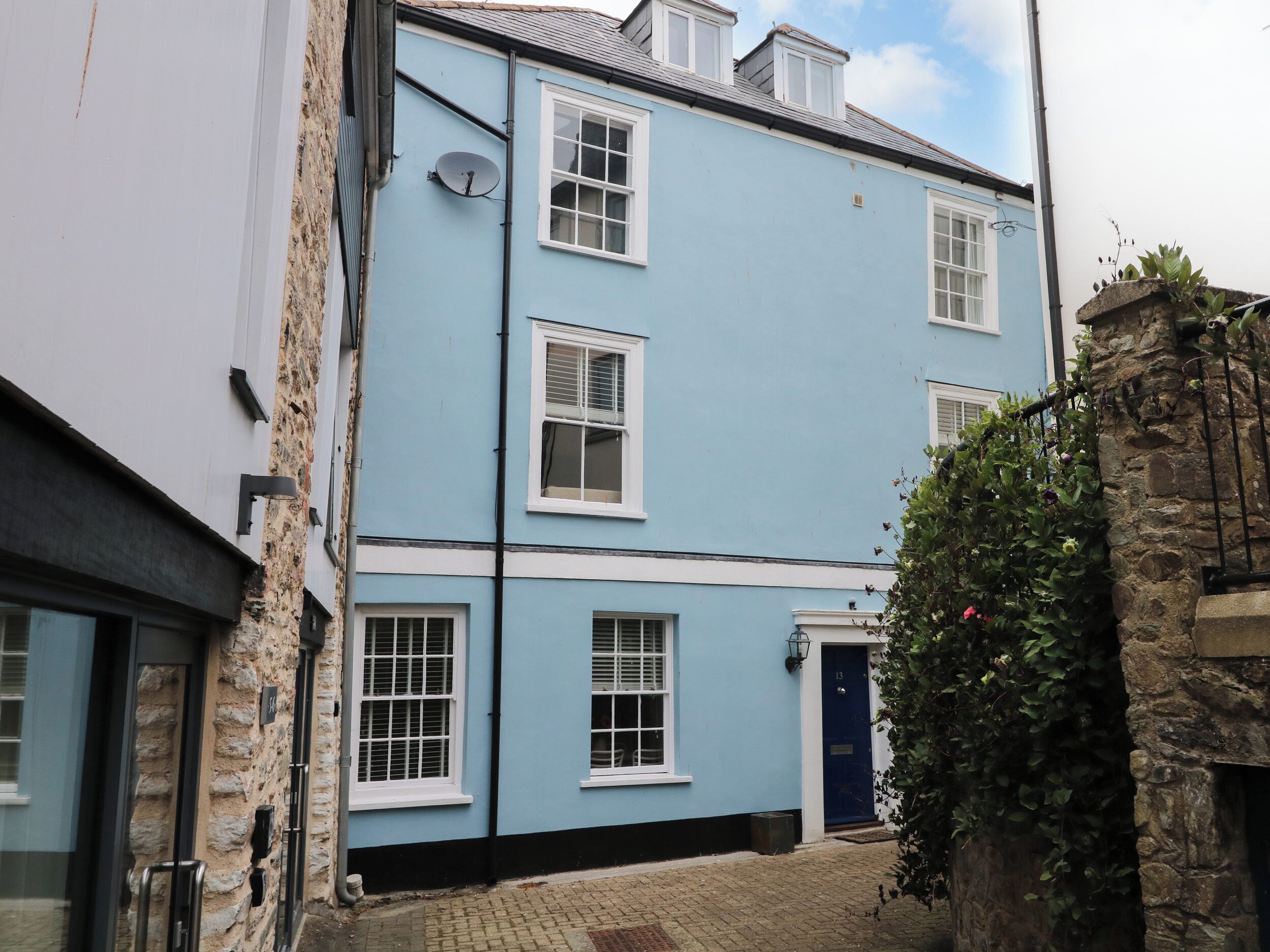 A two-story building with a blue facade, white window frames, and a stone wall.