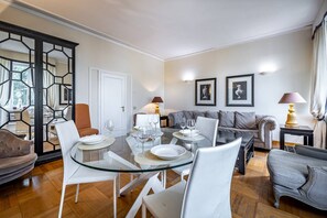 Una sala de estar moderna con una mesa de comedor de vidrio, sillas blancas, un sofá gris y un panel decorativo negro.