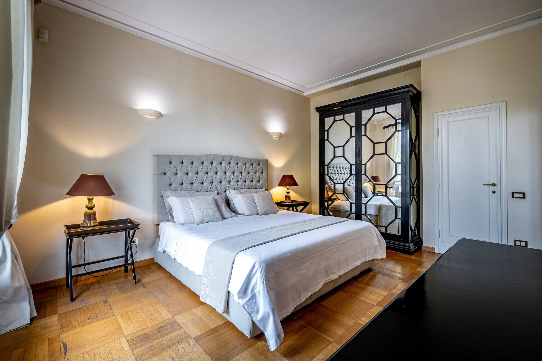 A neatly arranged bedroom with a large bed, two bedside tables with lamps, a wardrobe, and a wooden floor.