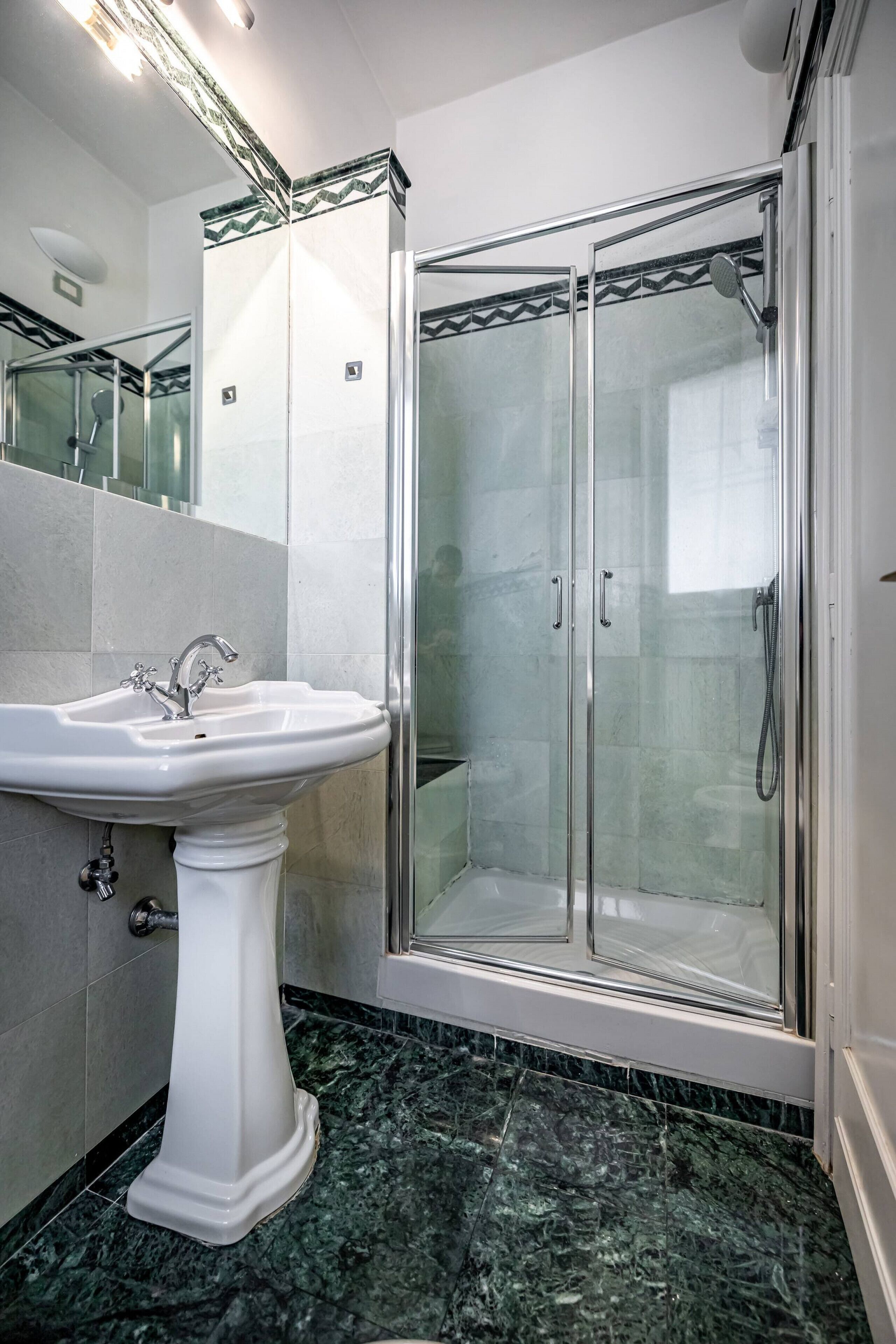 Ein Badezimmer mit einem Standwaschbecken, einer Duschkabine und einem gefliesten Boden.