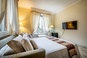 Una habitación de hotel con cama, dos mesitas de noche, un televisor y una ventana con cortinas.