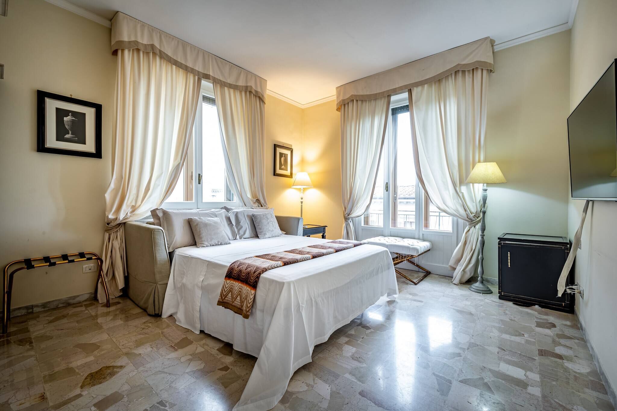 A hotel room with a large bed, two bedside tables, a chair, a desk, a lamp, and a TV.