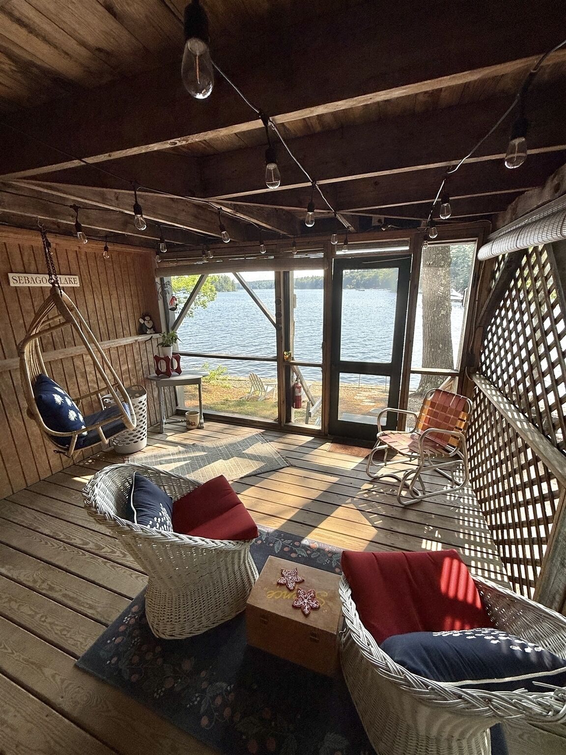 Uma cabana com interior de madeira, móveis de vime e vista para um lago.