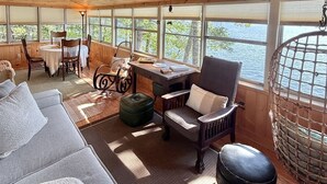 Ein geräumiges Zimmer mit Holzbalkendecke, großen Fenstern, einer Couch, einem Sessel, einem Tisch und einer Pendelleuchte.