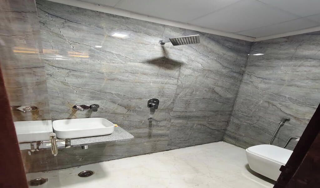 Een badkamer met een marmeren wand, een douche, een toilet en een wastafel.