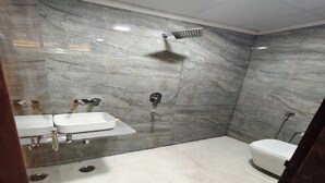 A bathroom with a marble wall, a shower, a toilet, and a sink. - Hotel Rudra Haridwar (Haridwar)