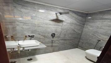 Een badkamer met een marmeren wand, een douche, een toilet en een wastafel.