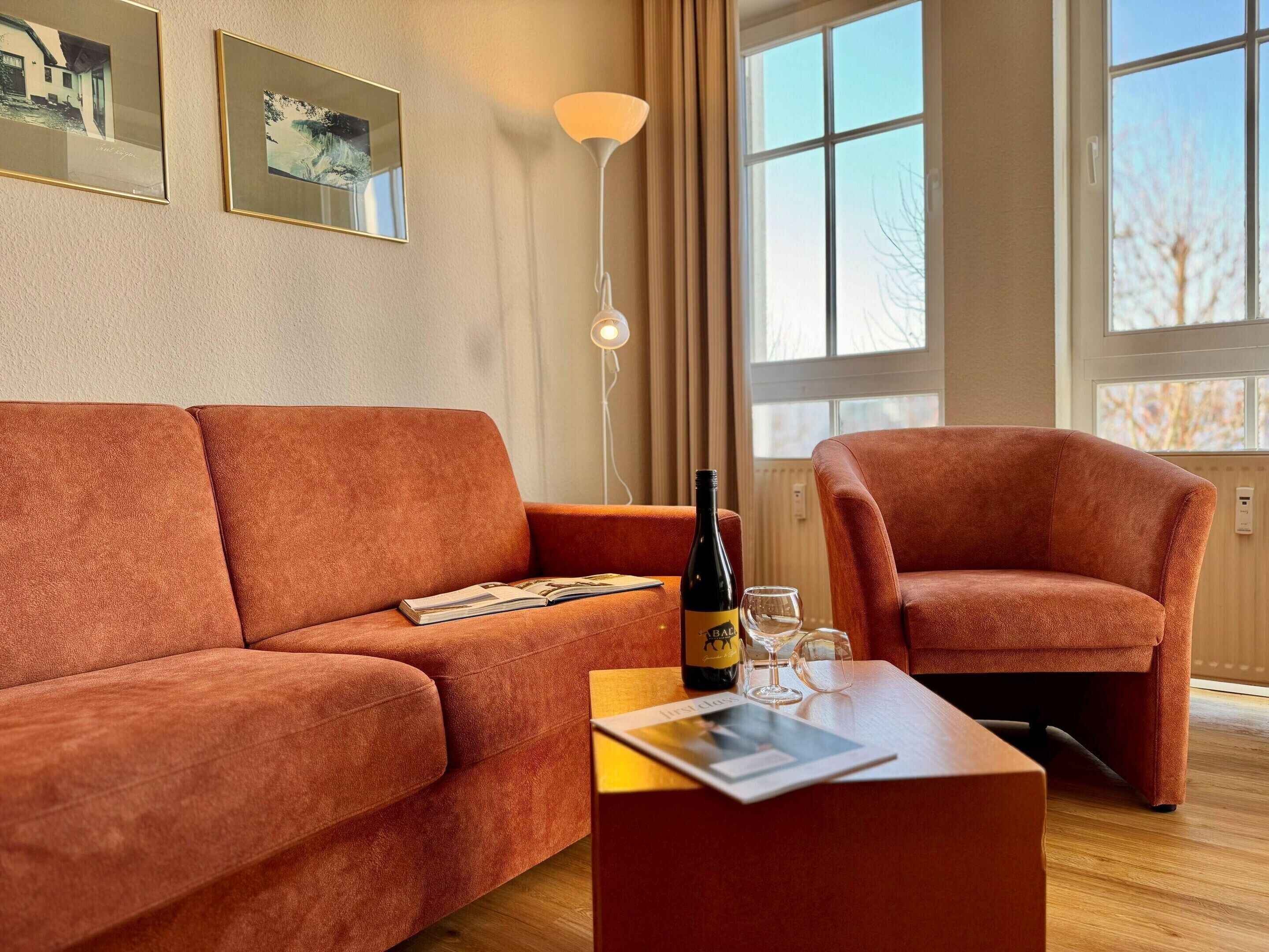 Ein modernes Wohnzimmer mit einer Couch, einem Sessel und einem Tisch mit Flasche und Glas.