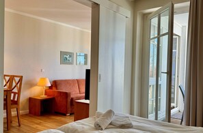 Ein Hotelzimmer mit Bett, einer Sitzecke, einem Schreibtisch, einer Lampe und einer Glastür zum Außenbereich.