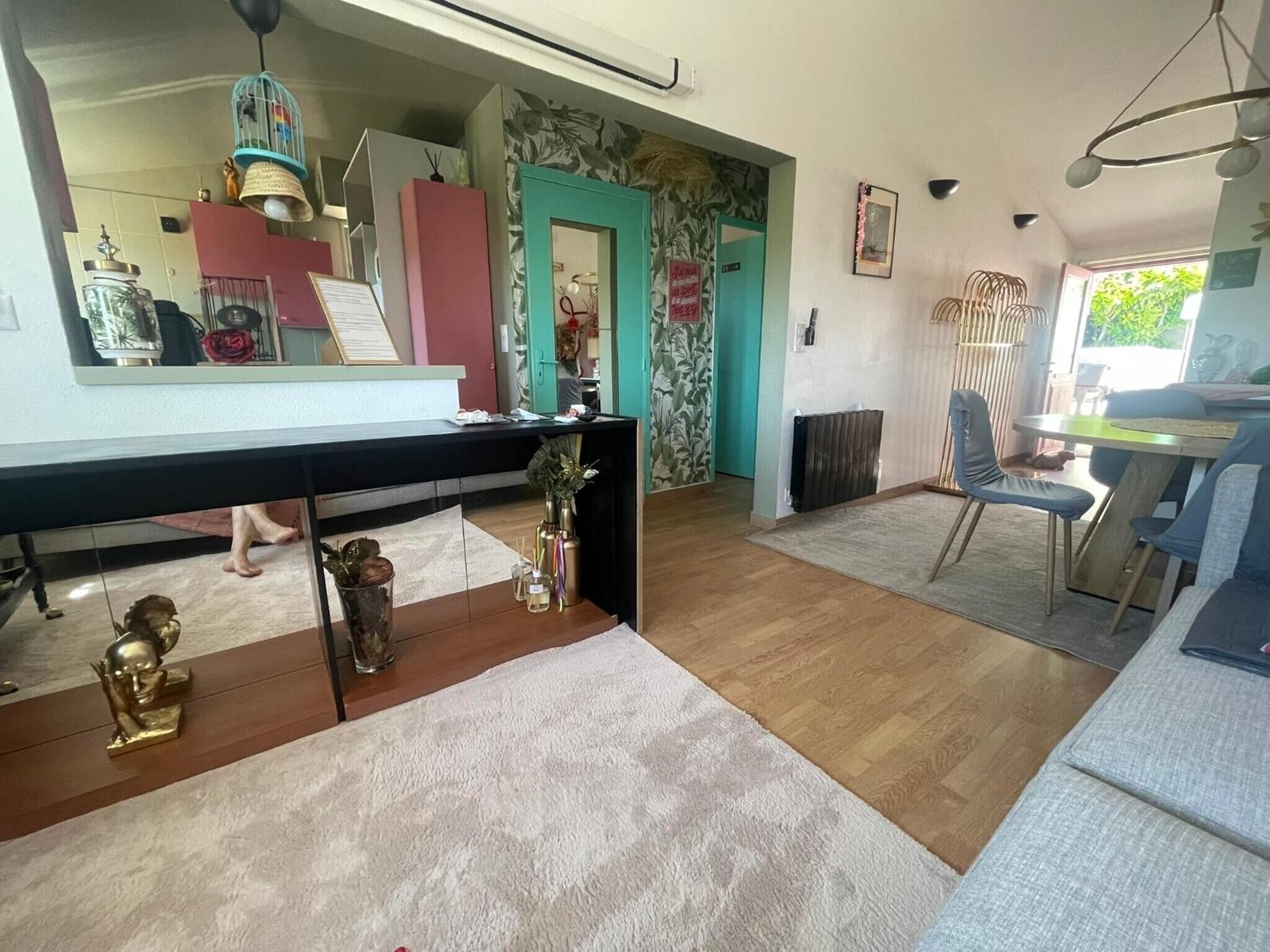 Ein modernes Wohnzimmer mit Holzboden, einem Essbereich mit Tisch und Stühlen, einer Küchenzeile mit Kühlschrank sowie einem Badezimmer mit Toilette und Waschbecken.