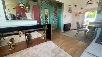 Ein modernes Wohnzimmer mit Holzboden, einem Essbereich mit Tisch und Stühlen, einer Küchenzeile mit Kühlschrank sowie einem Badezimmer mit Toilette und Waschbecken.