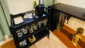 Ein Zimmer mit Fenster, ein Rollwagen mit Gläsern, eine kleine Pflanze und ein Tisch.