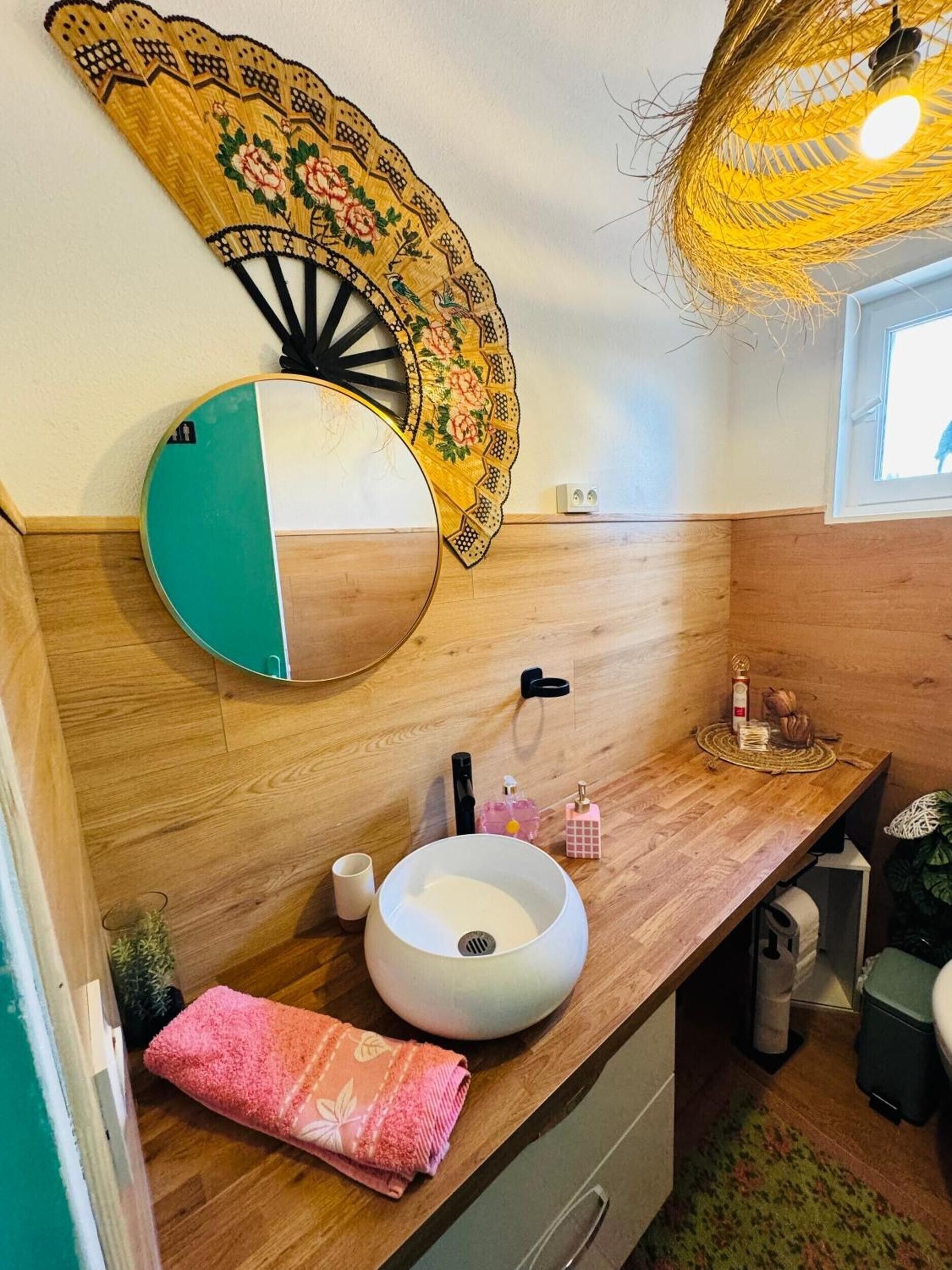 Un baño con tocador de madera, un espejo redondo, un lavabo y un abanico decorativo.
