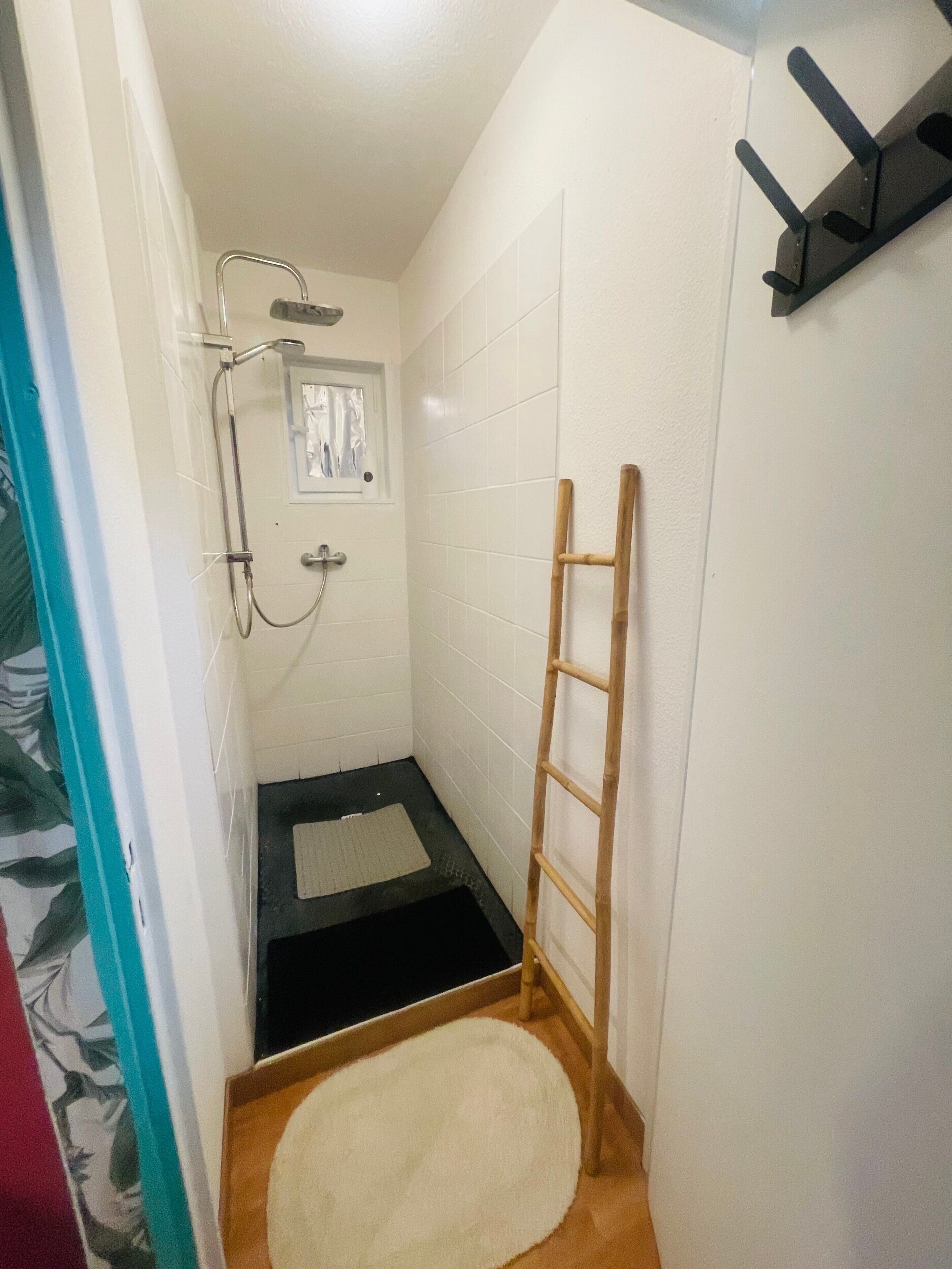 Un baño pequeño con ducha, una escalera de madera, un perchero para toallas y una ventana.